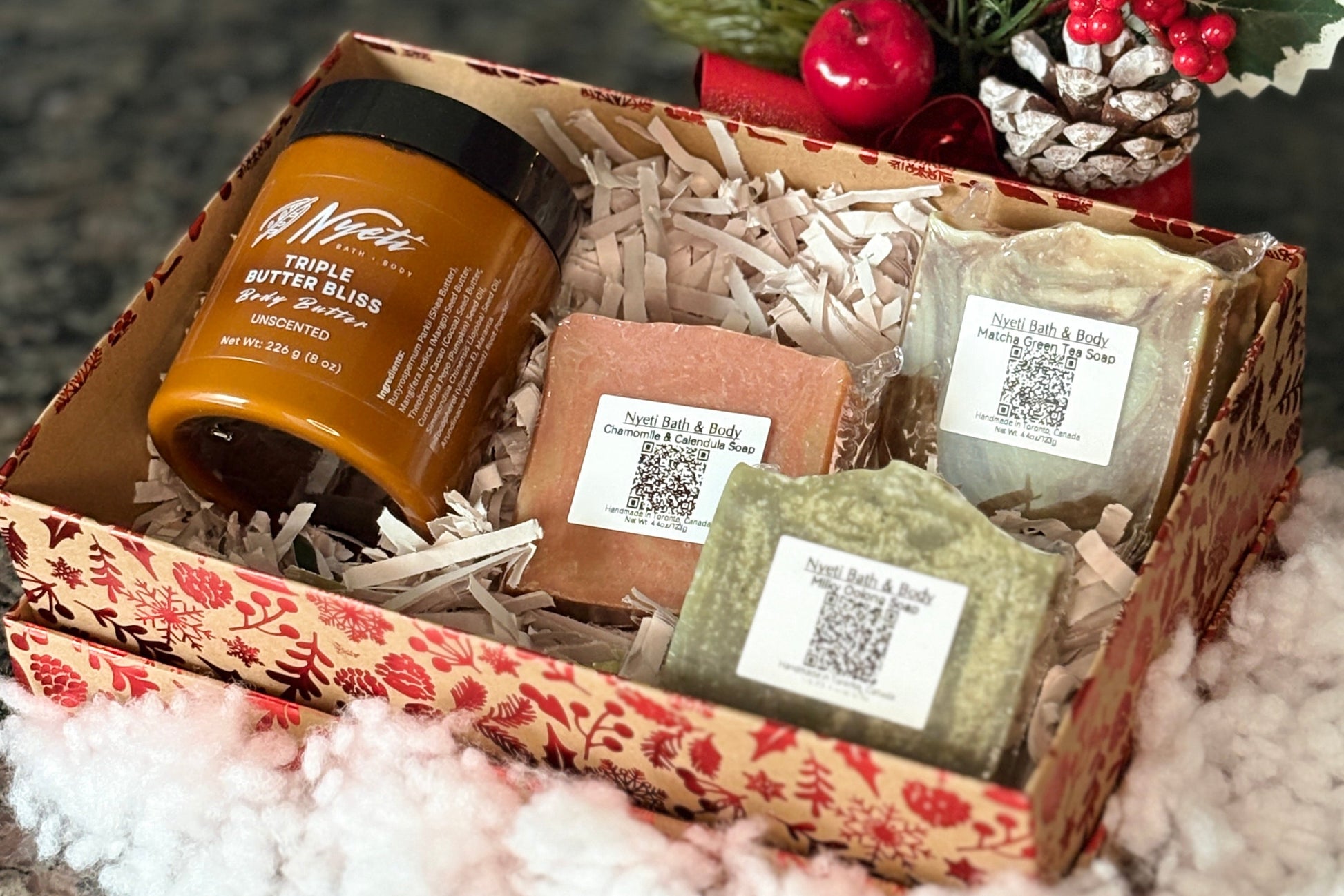 Gift set with body butter, soap bars, and a jar in a decorative box with Christmas decor.