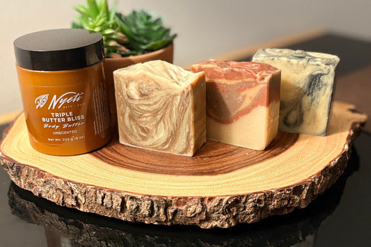 Body butter jar and three soap bars on a wooden surface with a plant in the background